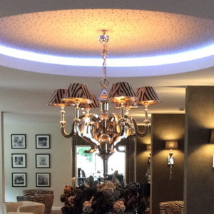 Eine elegante Kronleuchterbeleuchtung hängt von einer Decke mit LED-Ringlichtern in einem stilvoll eingerichteten Raum.